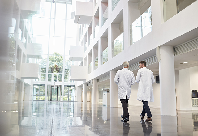 Rear View Of Doctors Talking As They Walk Through Hospital